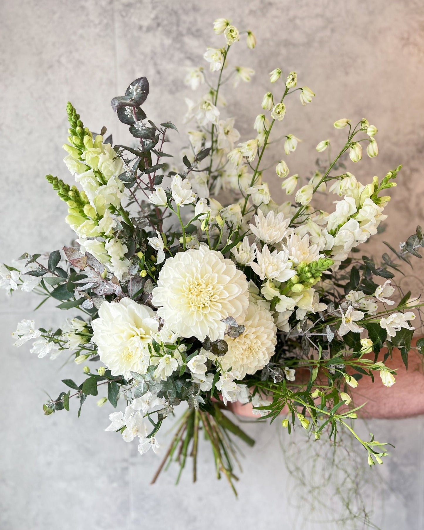 An elegant and classic, white hand tied bouquet of fresh flowers including dahlia, delphinium and seasonal blooms, available for same day flower delivery in Melton and surrounding areas by The Flowered Heart