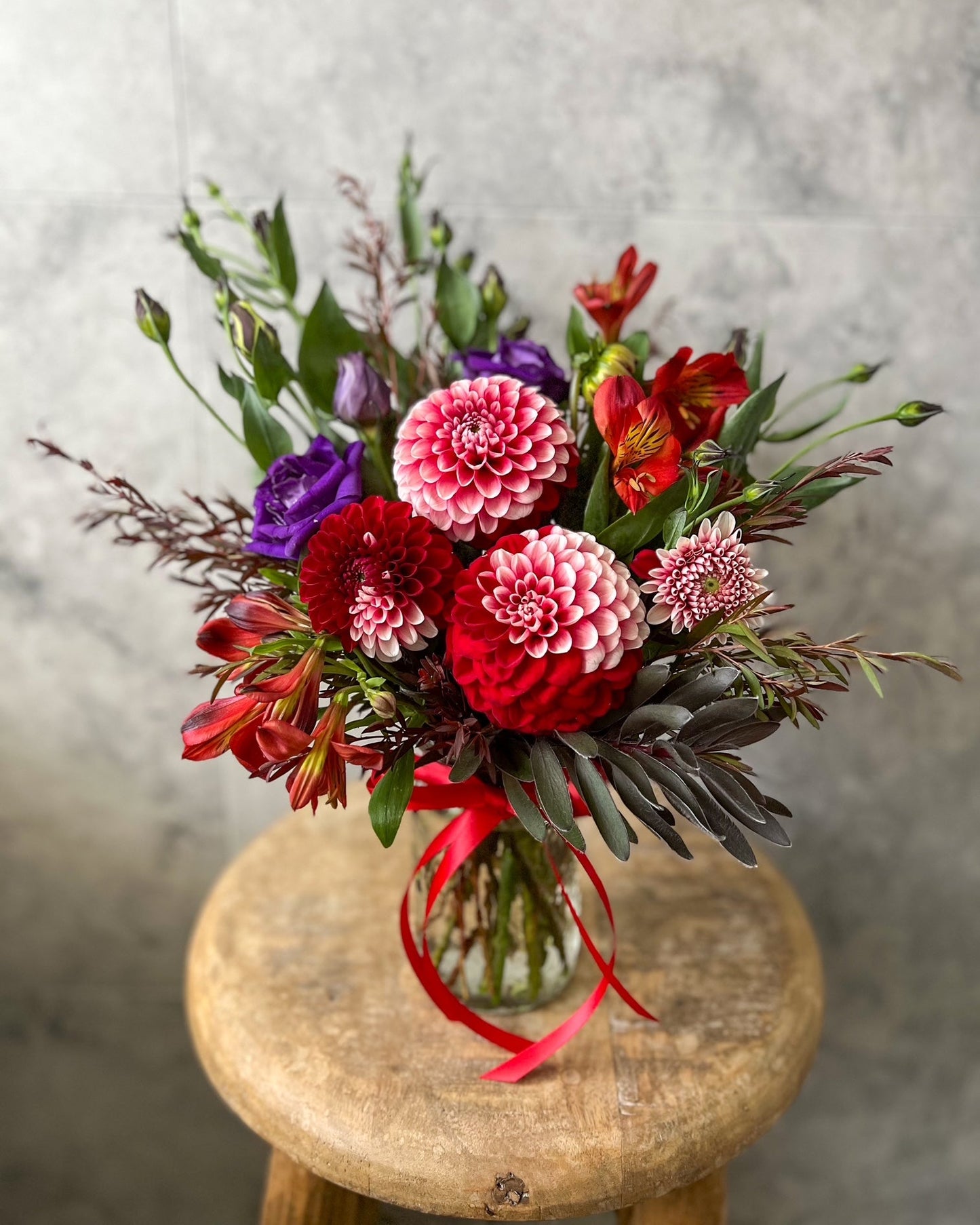 A bold, jar arrangement of fresh flowers including red dahlias and seasonal blooms, available for same day flower delivery in Melton by The Flowered Heart